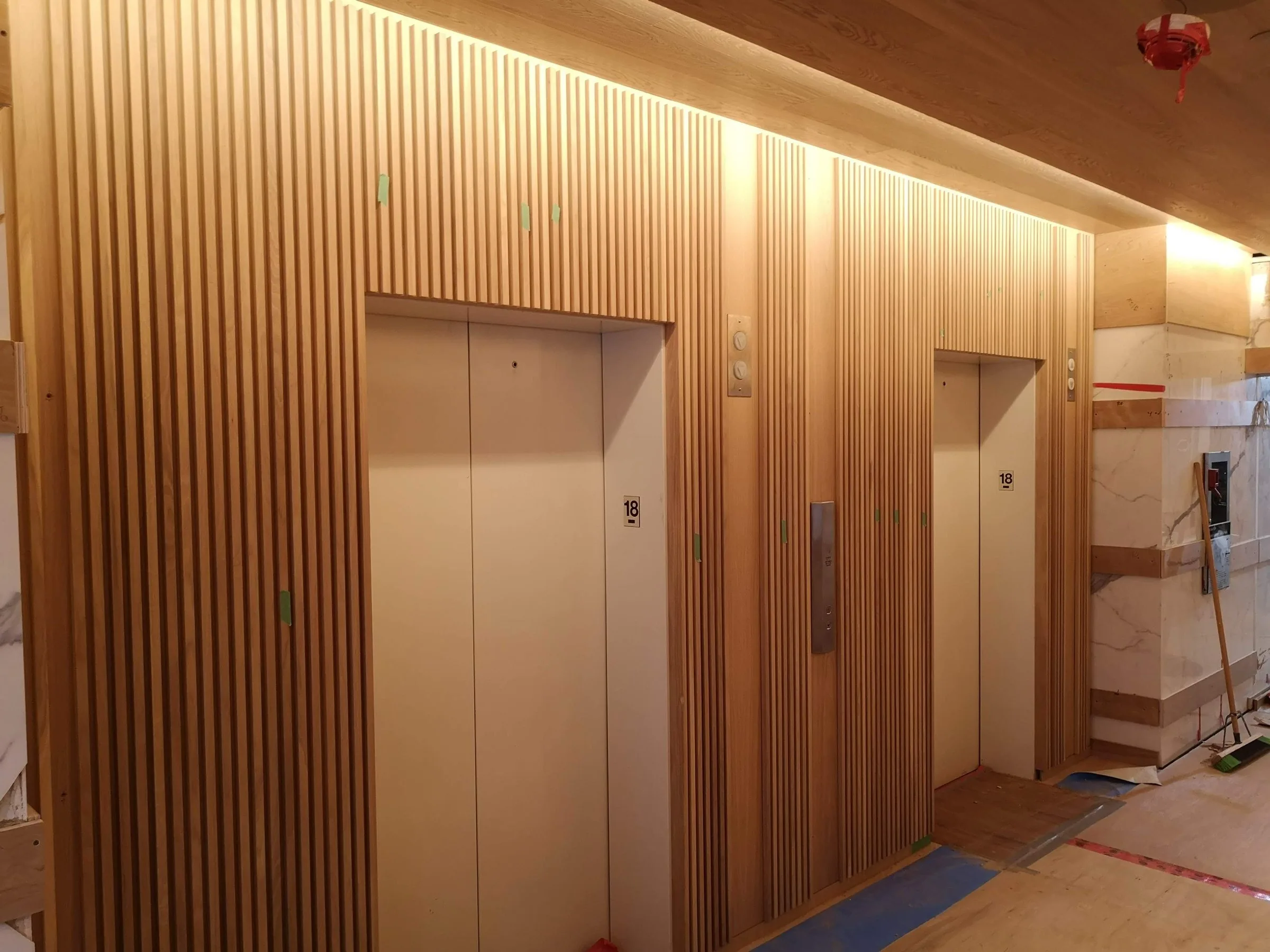 A slatted white-oak wall wrapping an elevator lobby, finished against marble